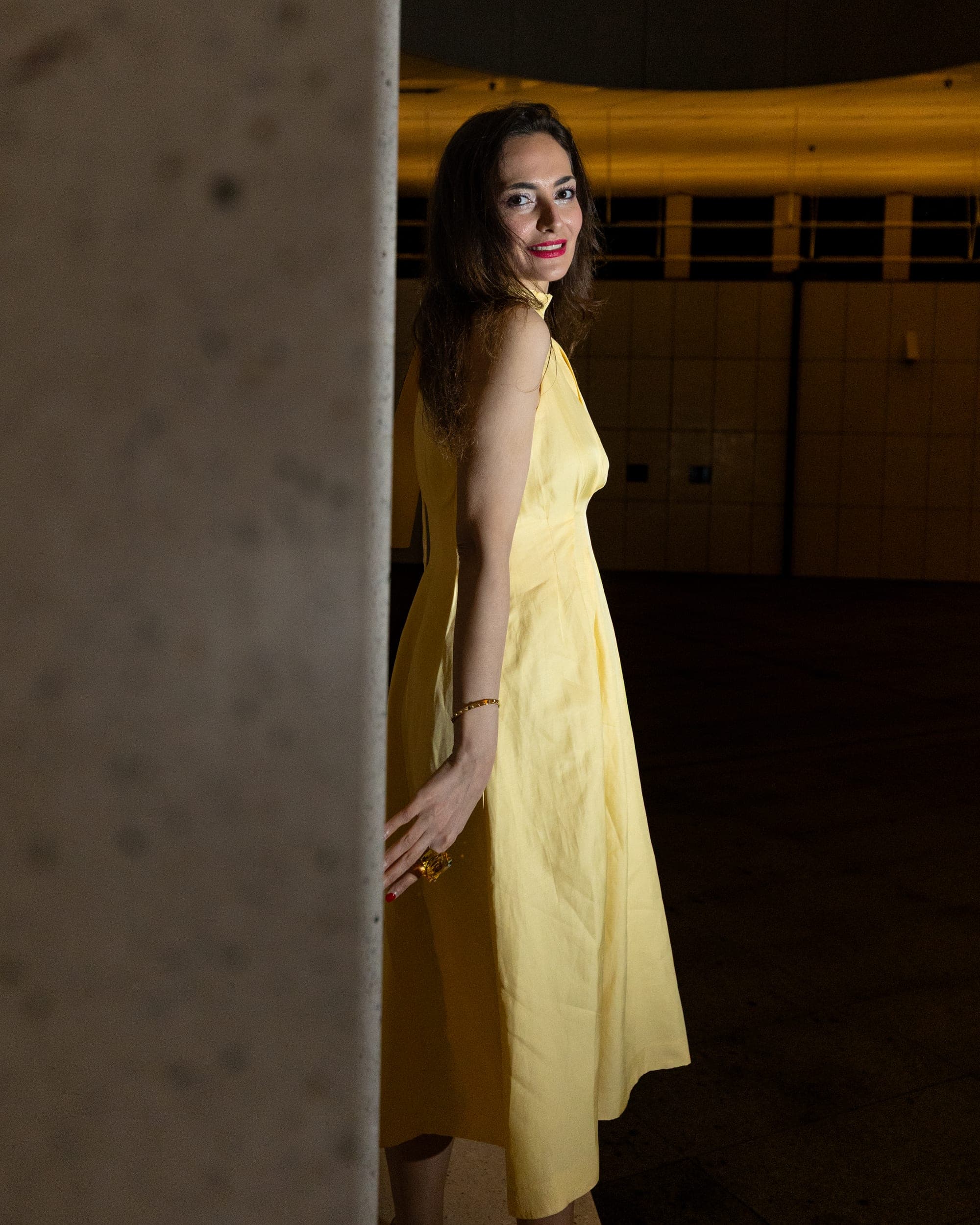 Model in a yellow dress smiling beside a concrete column at night, Sydney fashion editorial