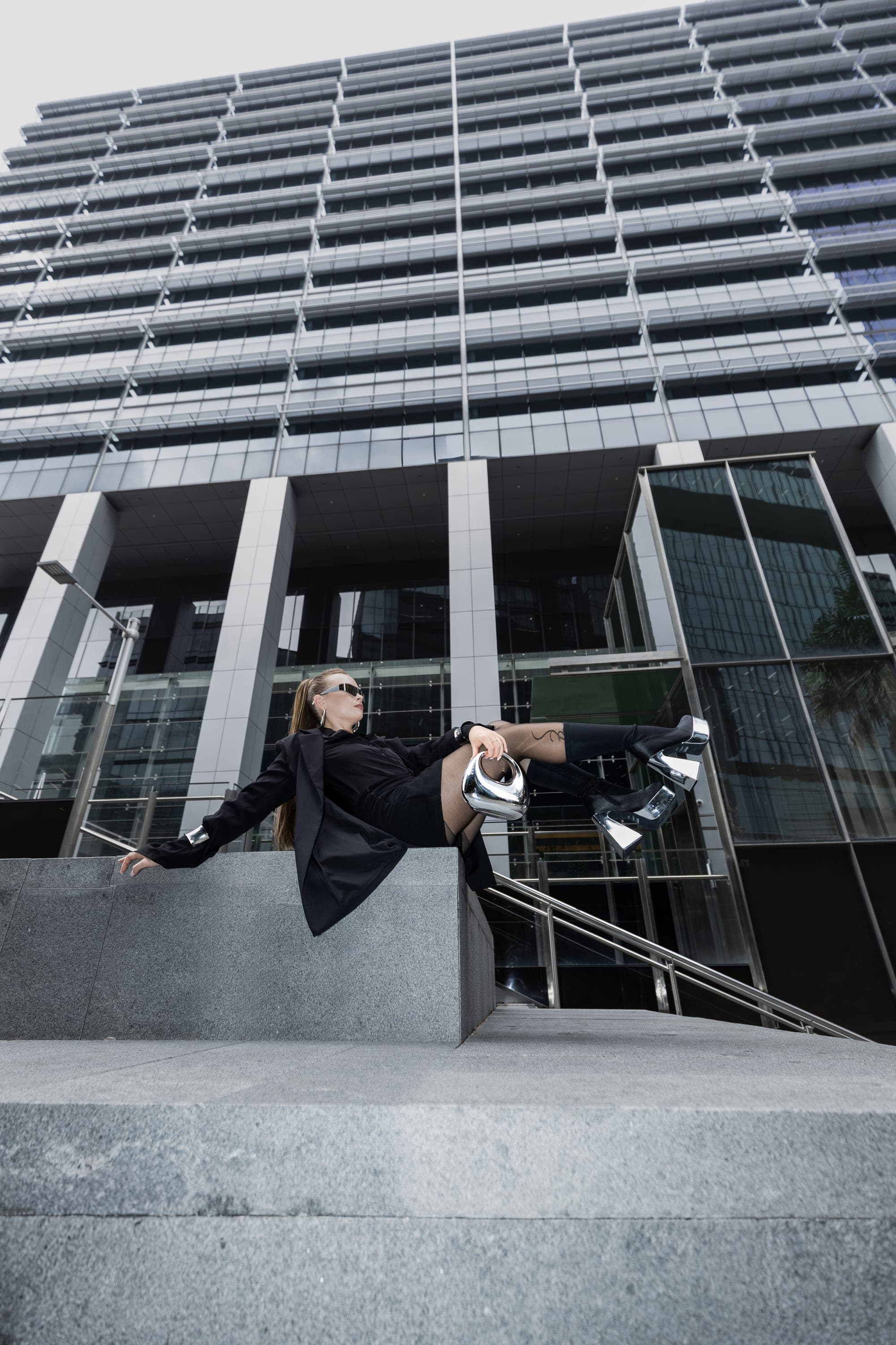 Model reclining on a ledge with a silver handbag, Sydney CBD street fashion editorial