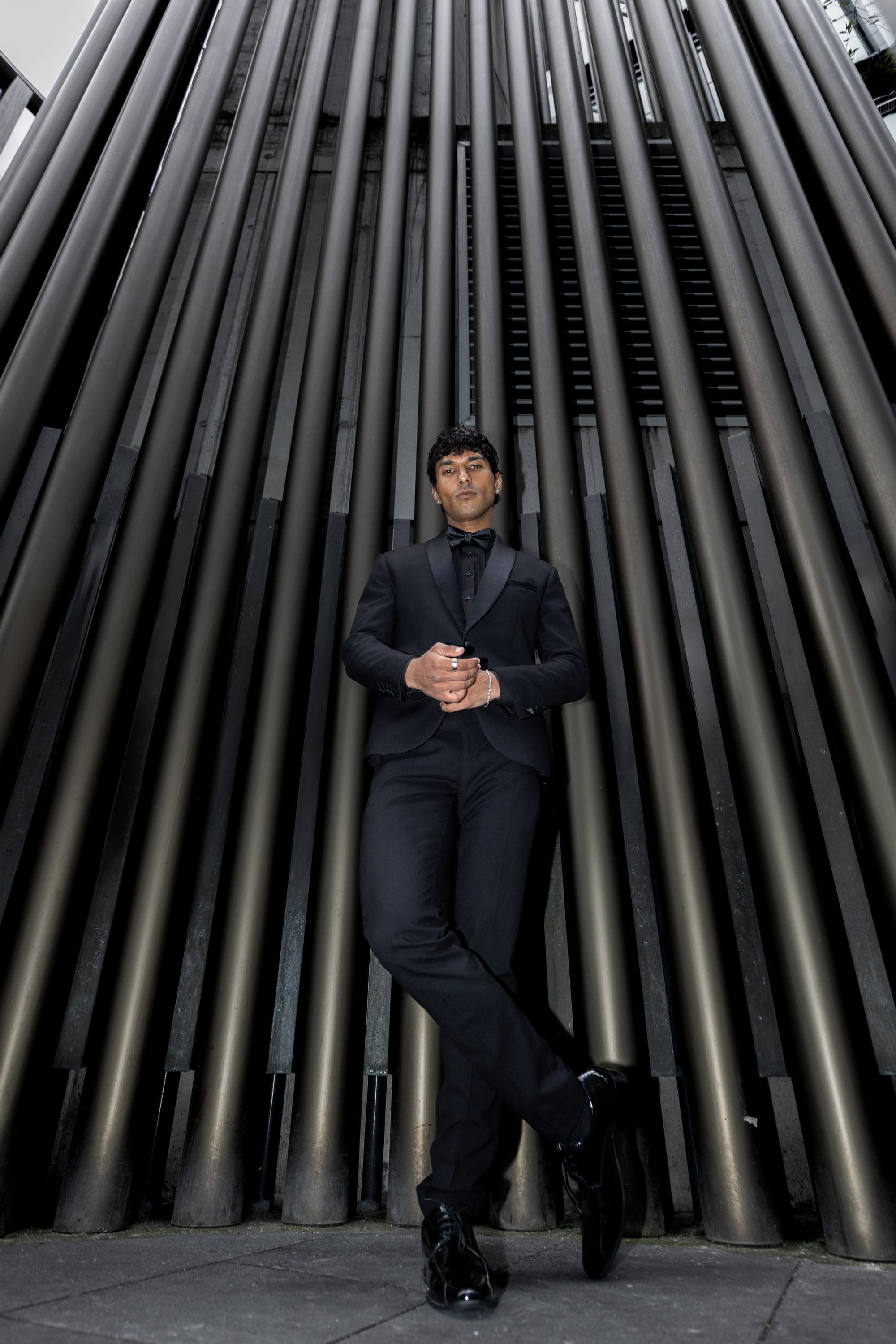 Man in a black tuxedo against metallic pipe architecture, Sydney menswear street photography