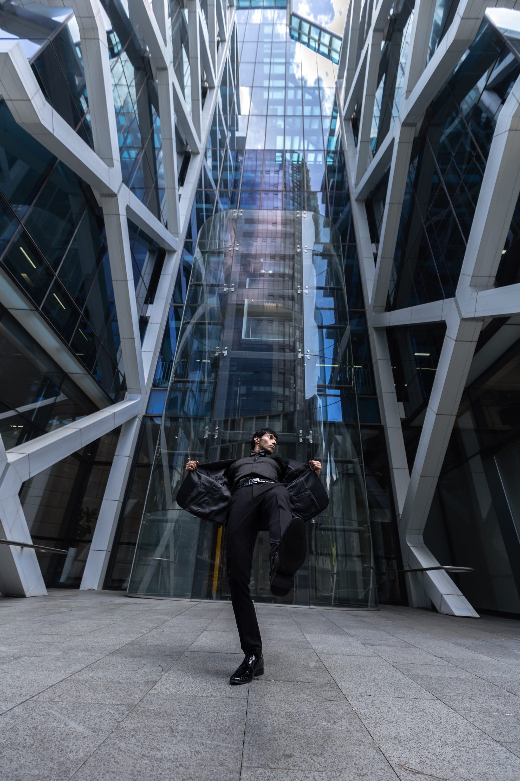 Man in a black suit mid-motion against a modern glass building facade, Sydney street fashion