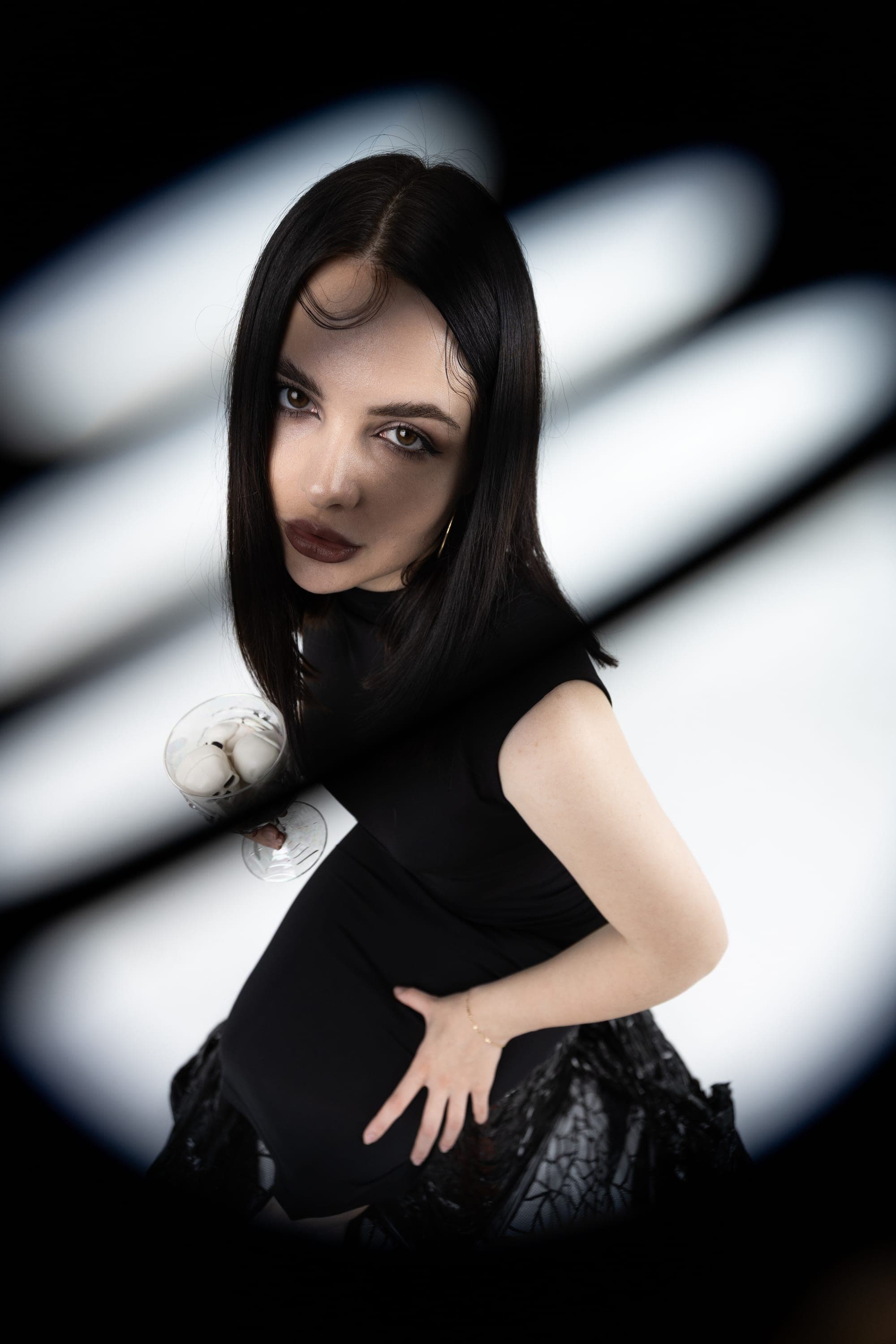 Model in a black dress holding a martini glass, studio photography with light-panel background