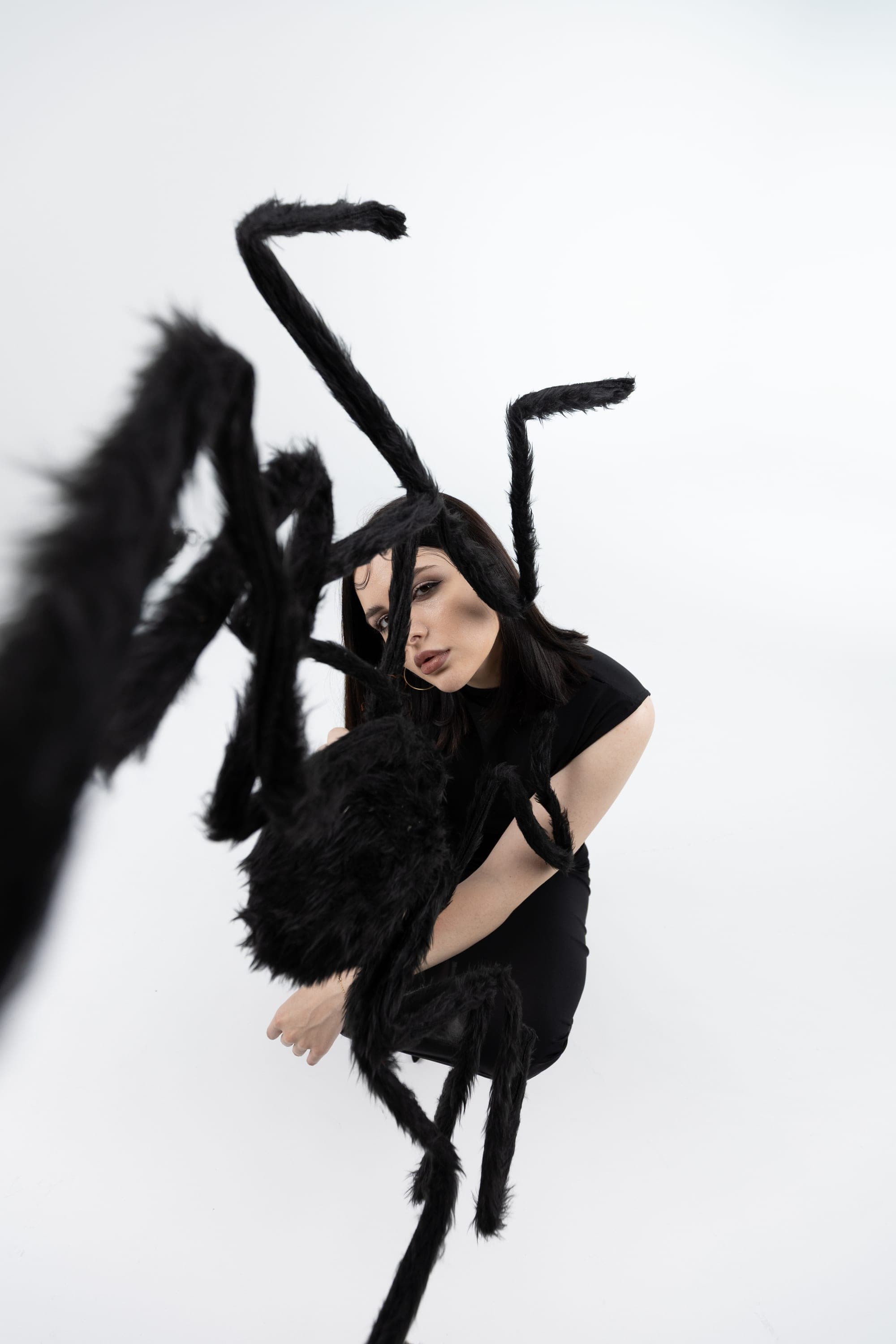 Model in a black dress with a giant black spider prop on a white studio backdrop