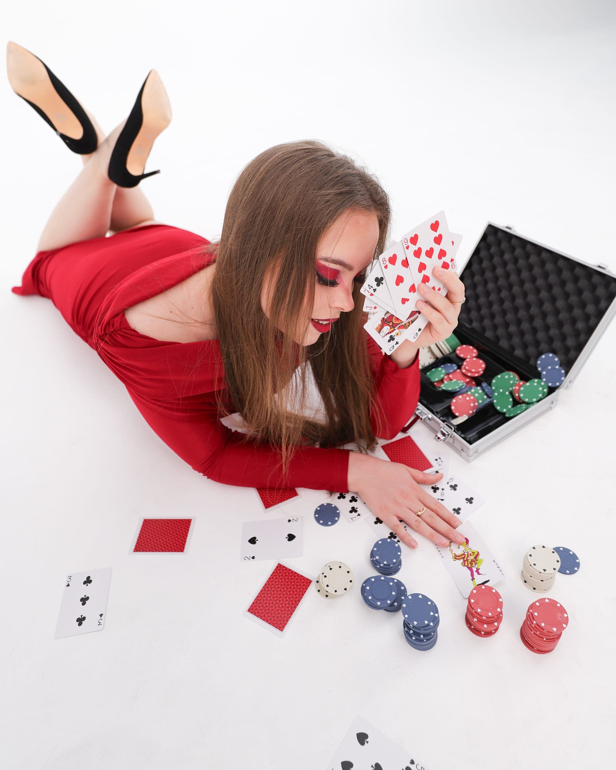 Model in a red dress lying among playing cards and poker chips, studio photography